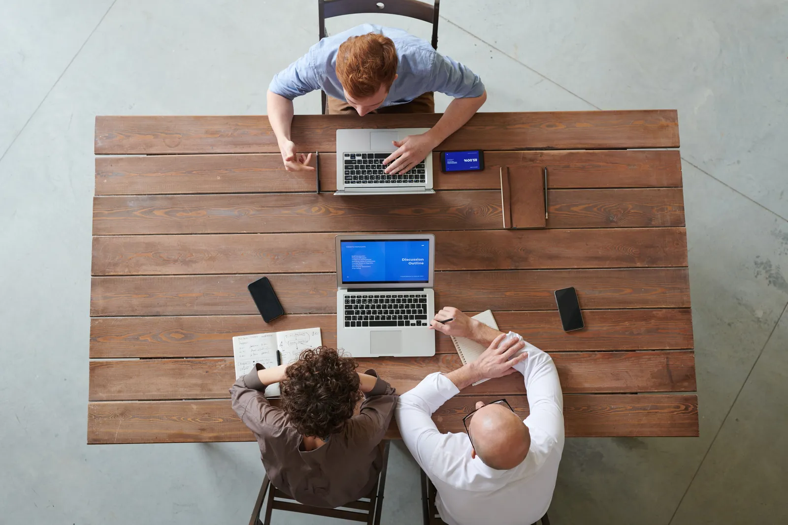 A team of three professionals collaborating at a wooden table with laptops and smartphones in a modern office