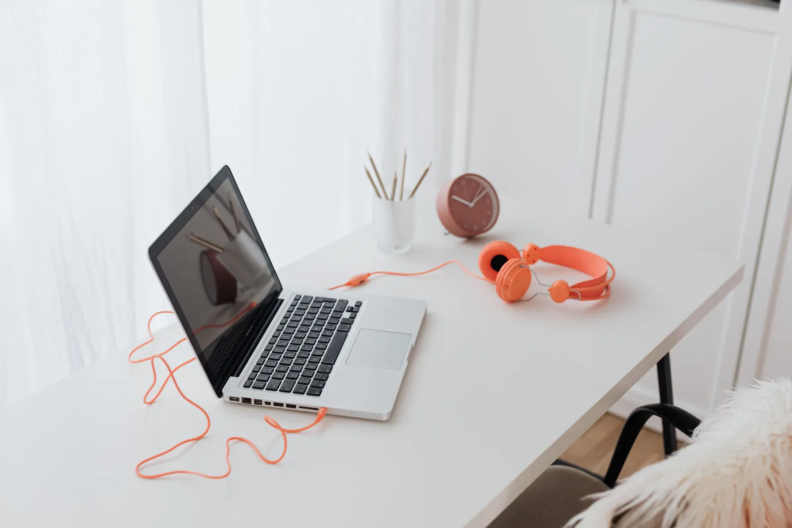 Minimalist workspace featuring a laptop and orange headphones on a clean white desk