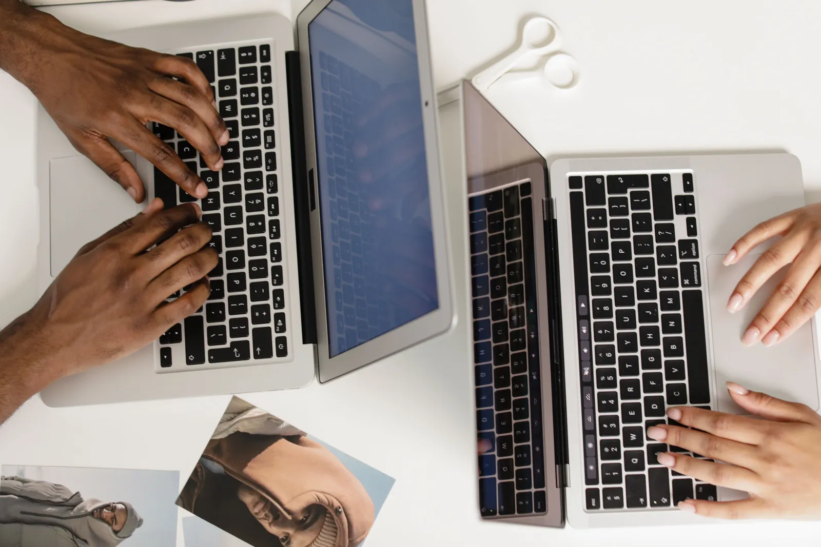 Two hands typing on laptops on a white desk, viewed from above, fostering teamwork
