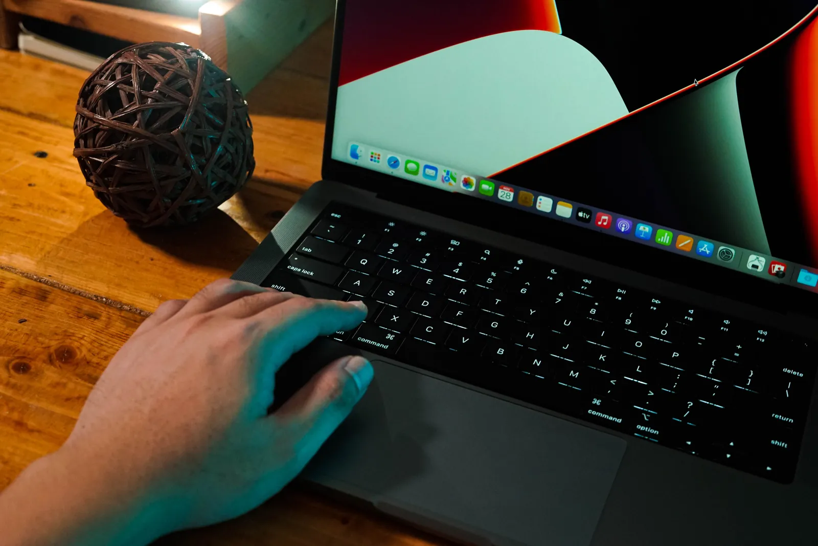 A hand interacting with a laptop on a wooden desk, next to a decorative ball
