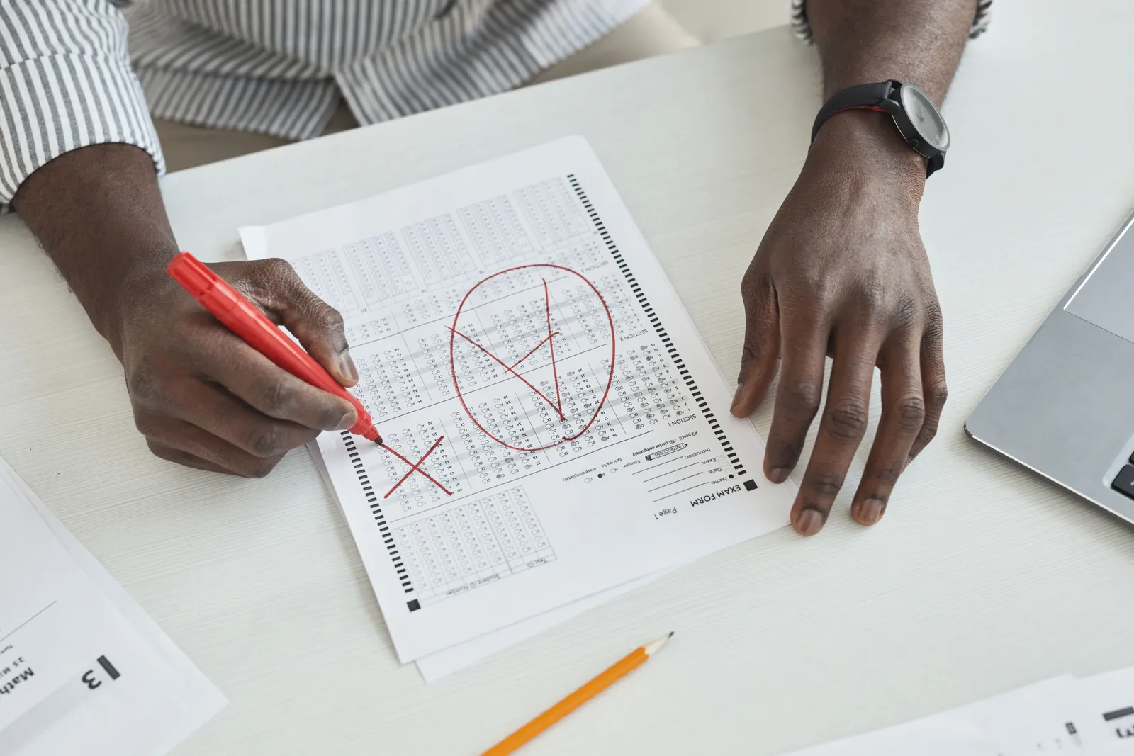 Close-up of a teacher marking a test paper with a red marker on a desk