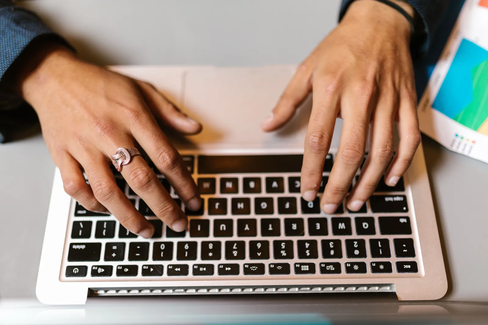 Hands typing on a laptop with a ring, emphasizing technology and work