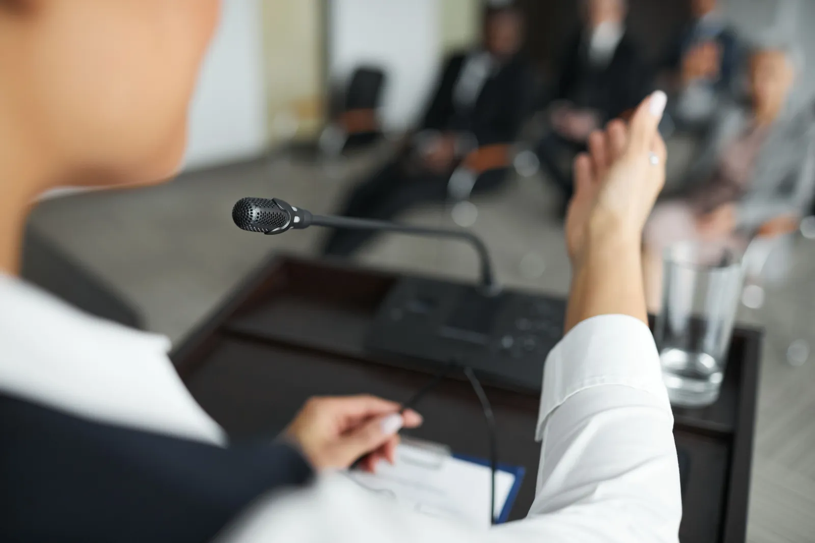 A person speaking at a podium with a microphone to an audience during a business meeting