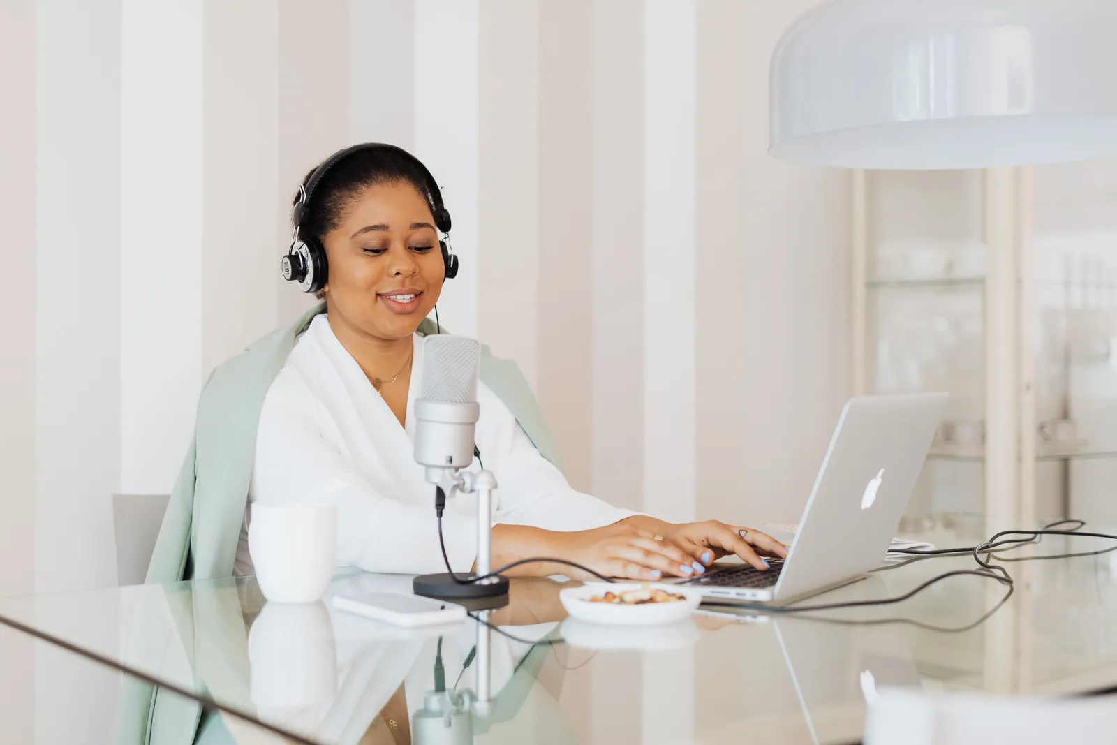 Smiling woman using laptop and microphone at glass desk, perfect for home office stock photos