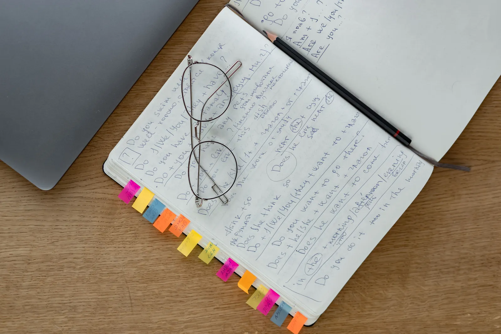 Top view of a notebook with handwritten notes, eyeglasses, and a pencil on a wooden desk