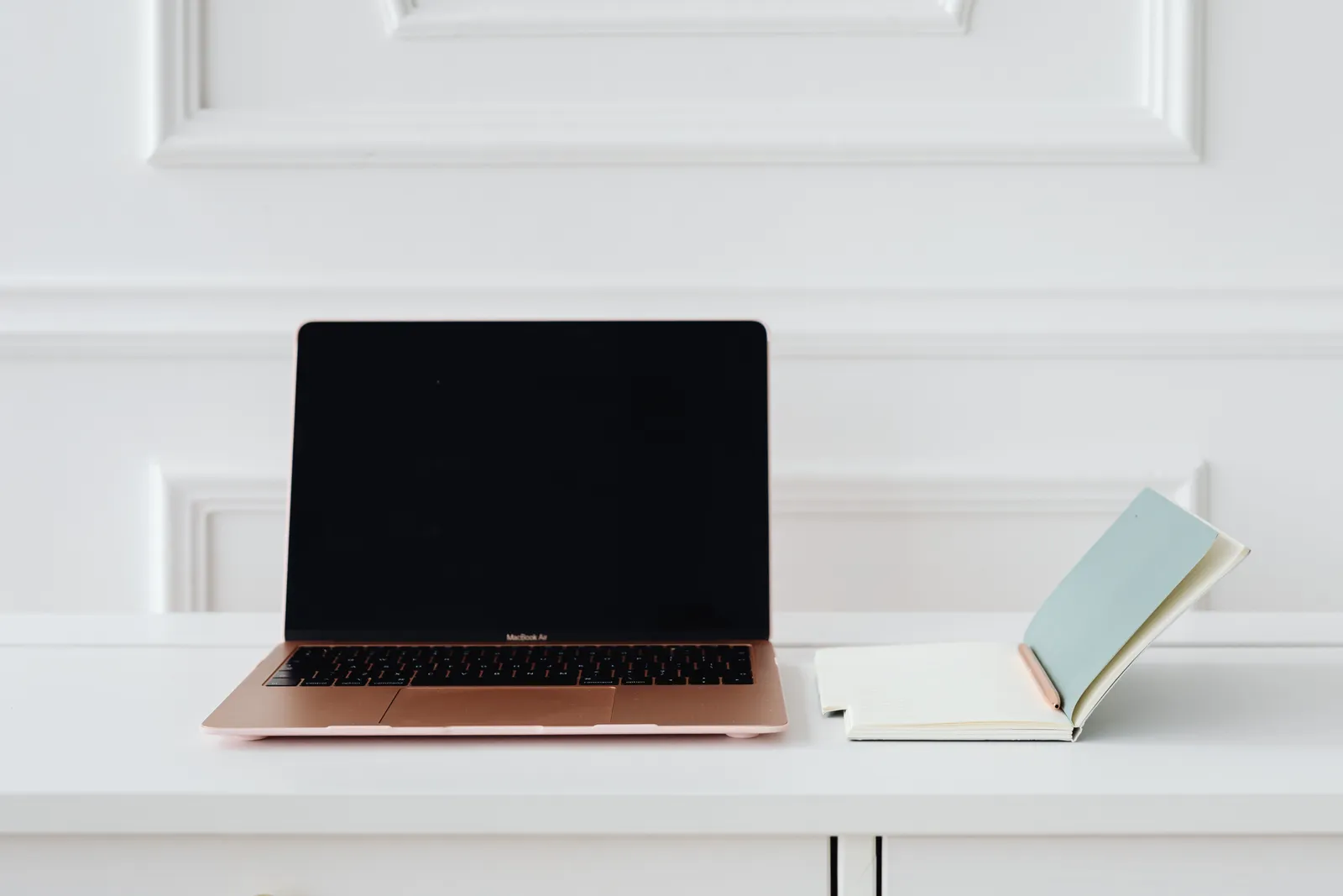 A clean, minimalist desk setup with a gold laptop and open notebook, perfect for productivity