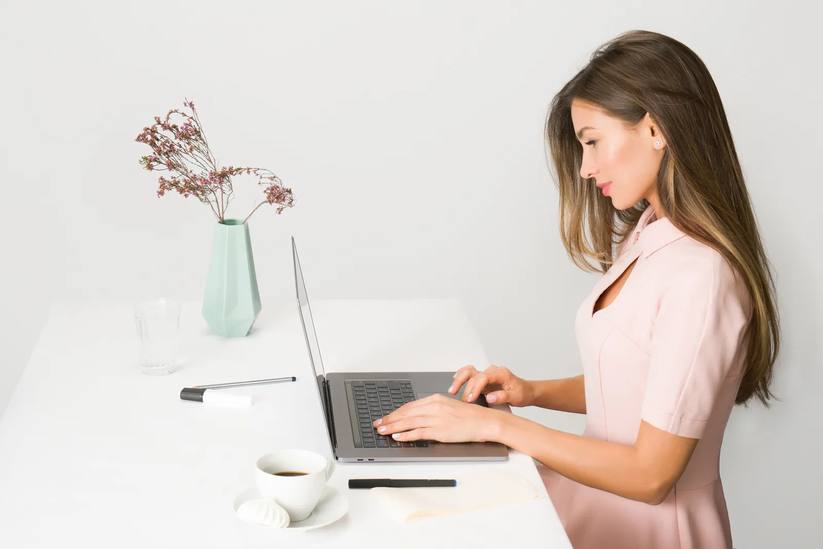 A woman in a pink dress working on a laptop at a modern, minimalist desk