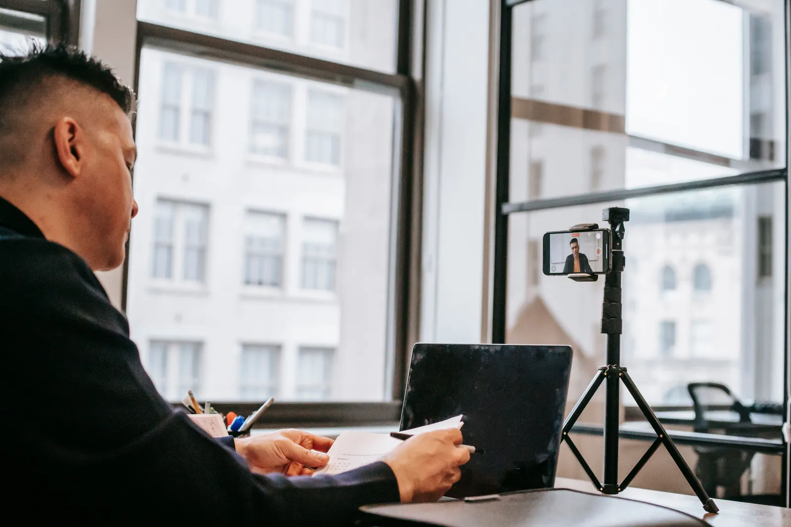 Business professional on video call setup with laptop and smartphone tripod