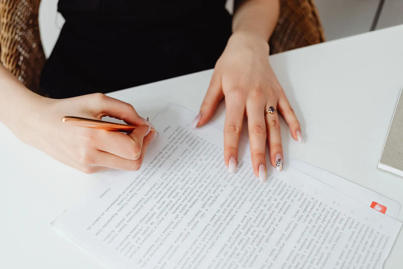 A woman signing a document with a pen on a desk, emphasizing hands and writing