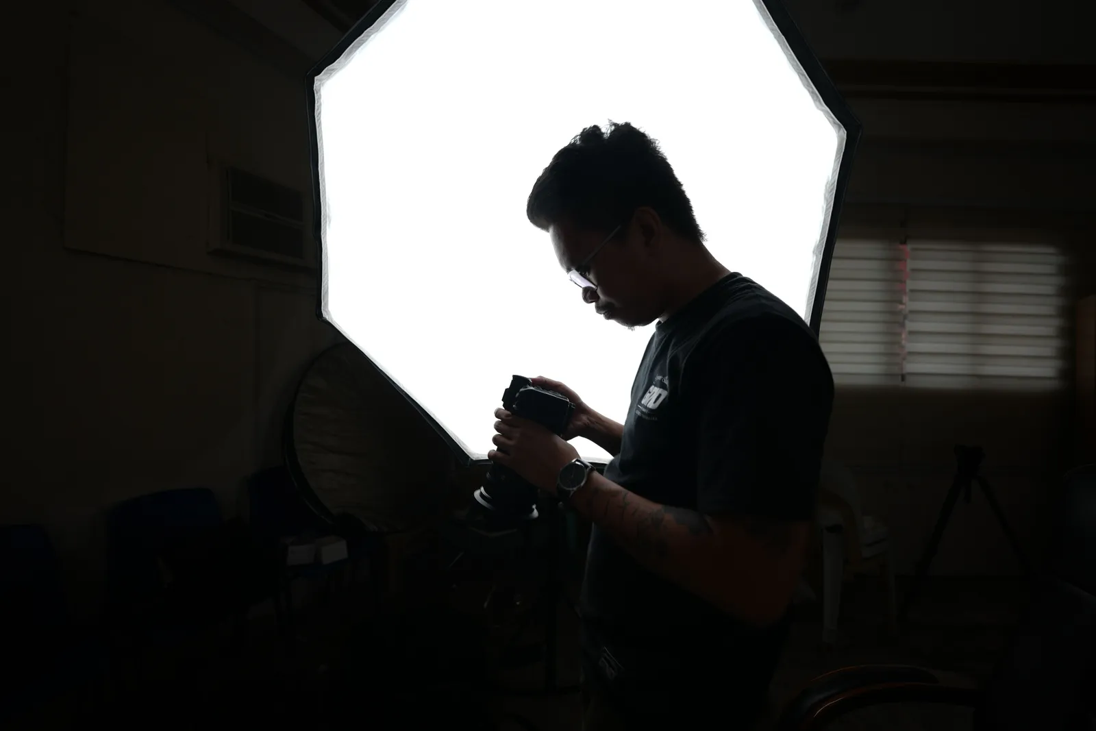 Professional photographer adjusting camera settings in a dimly lit studio with softbox lighting