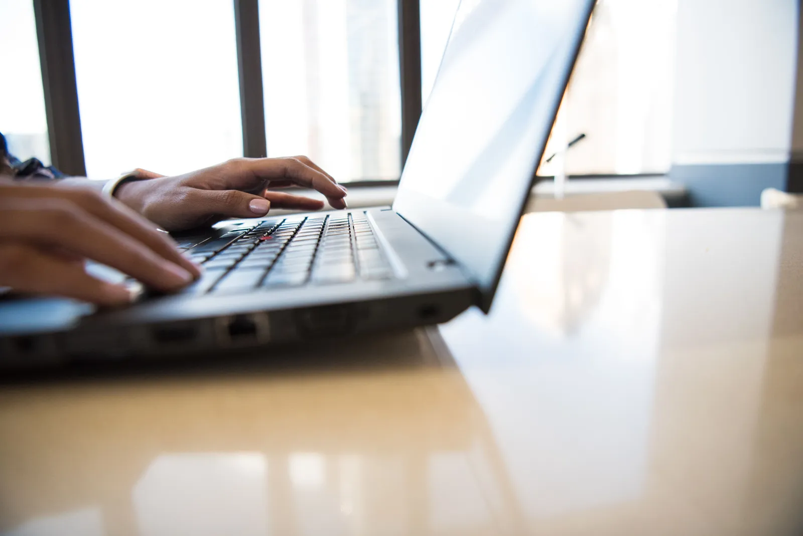 Close-up of woman's hands typing on a laptop in a bright, modern office environment