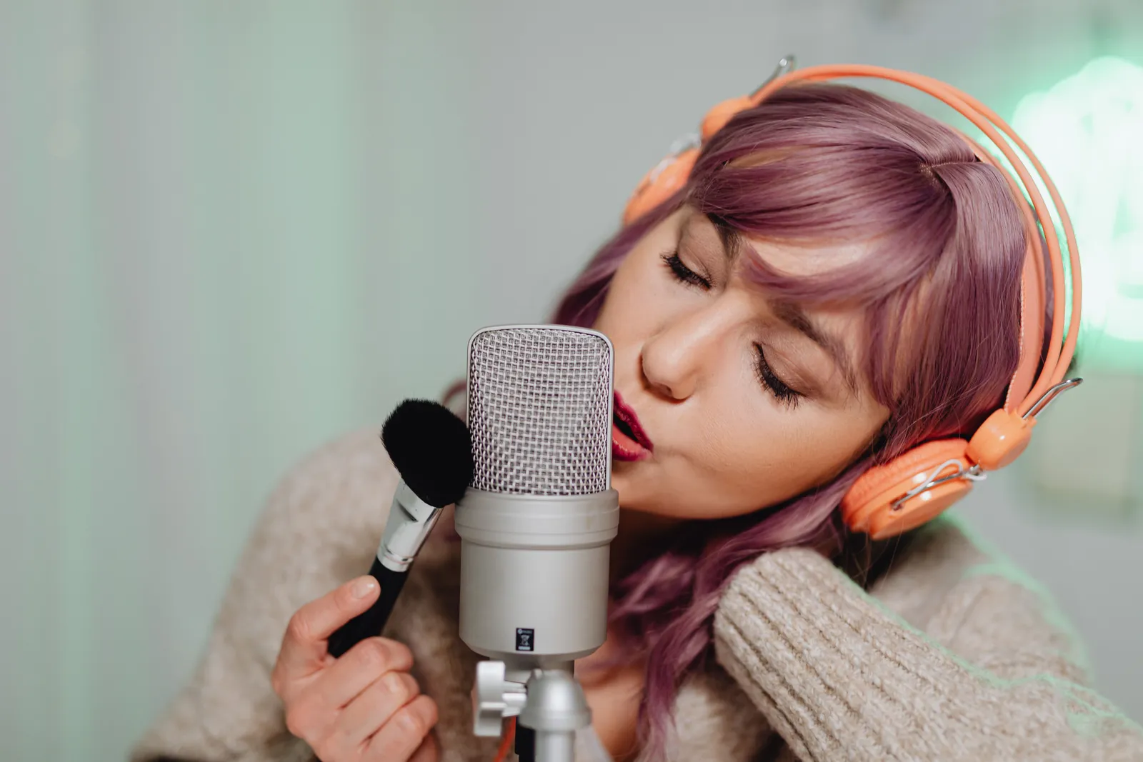 Woman wearing headphones performs ASMR with a microphone and brush indoors