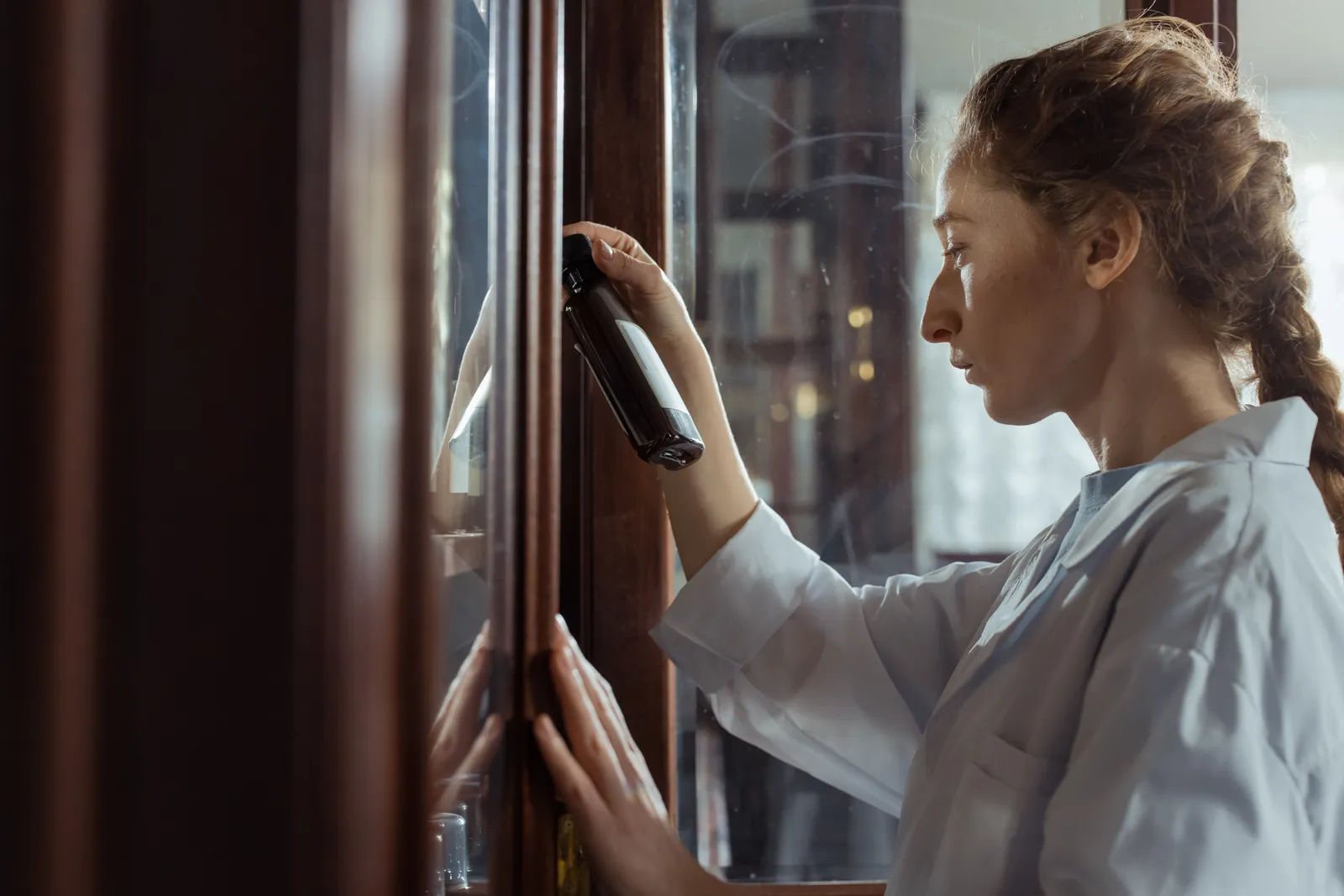 Focused woman inspecting cabinet with bottle in hand, indoors
