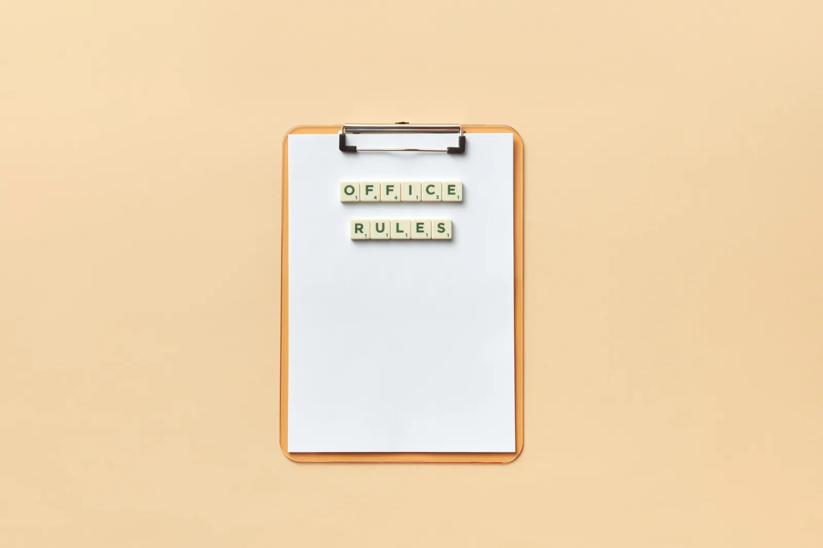 A clipboard with the phrase 'Office Rules' spelled out using Scrabble tiles on a beige background