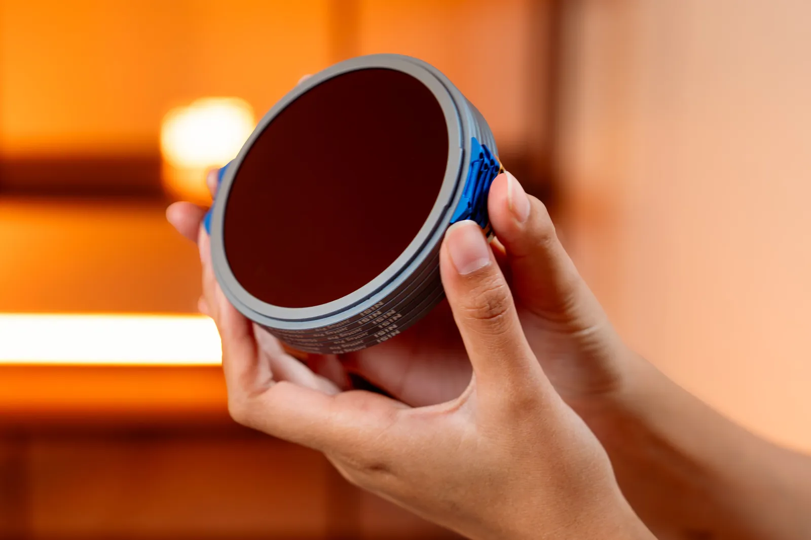 Hands holding a circular camera lens filter against a soft, warm background