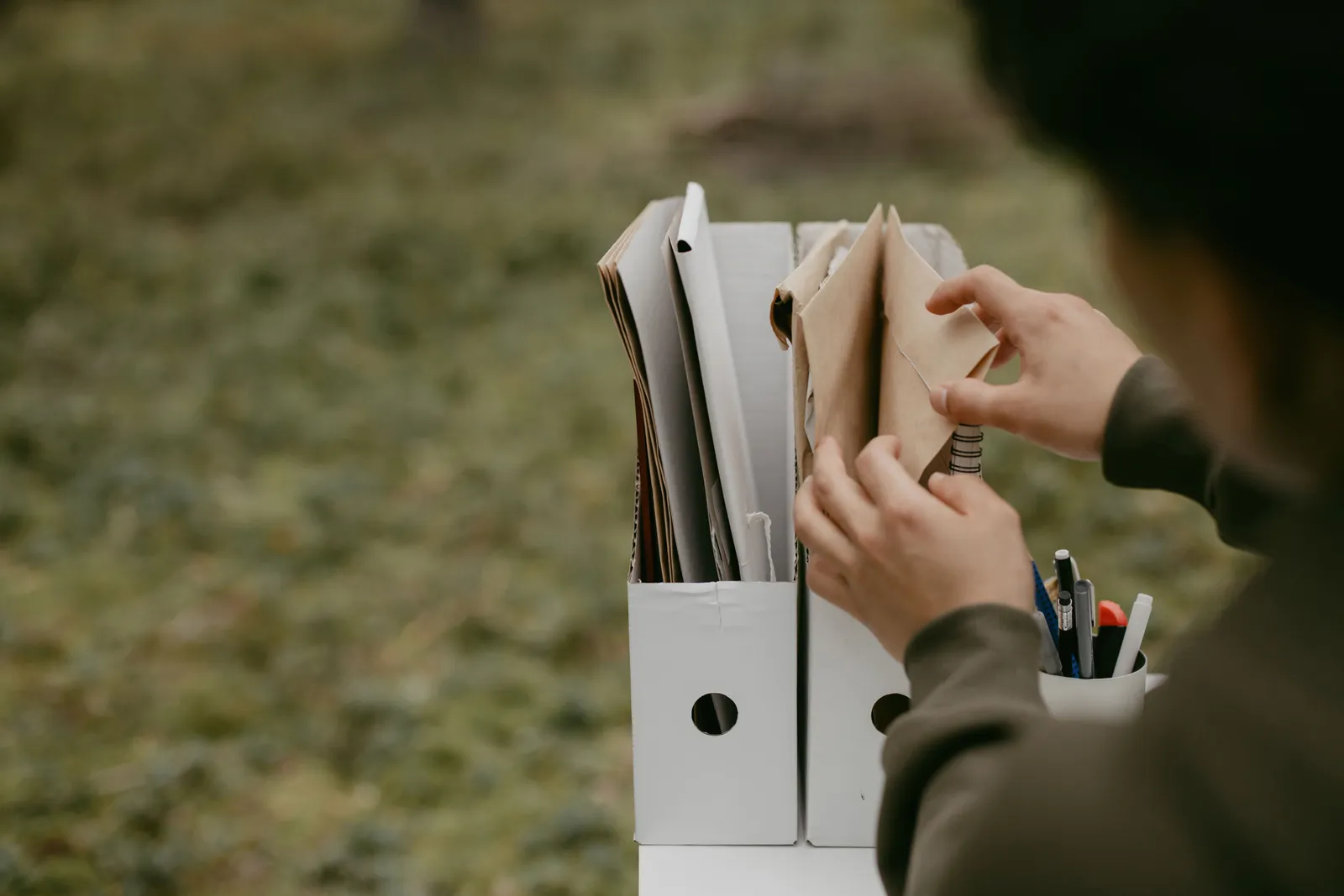 Person sorting documents in folders outdoors, hands visible, neutral tone