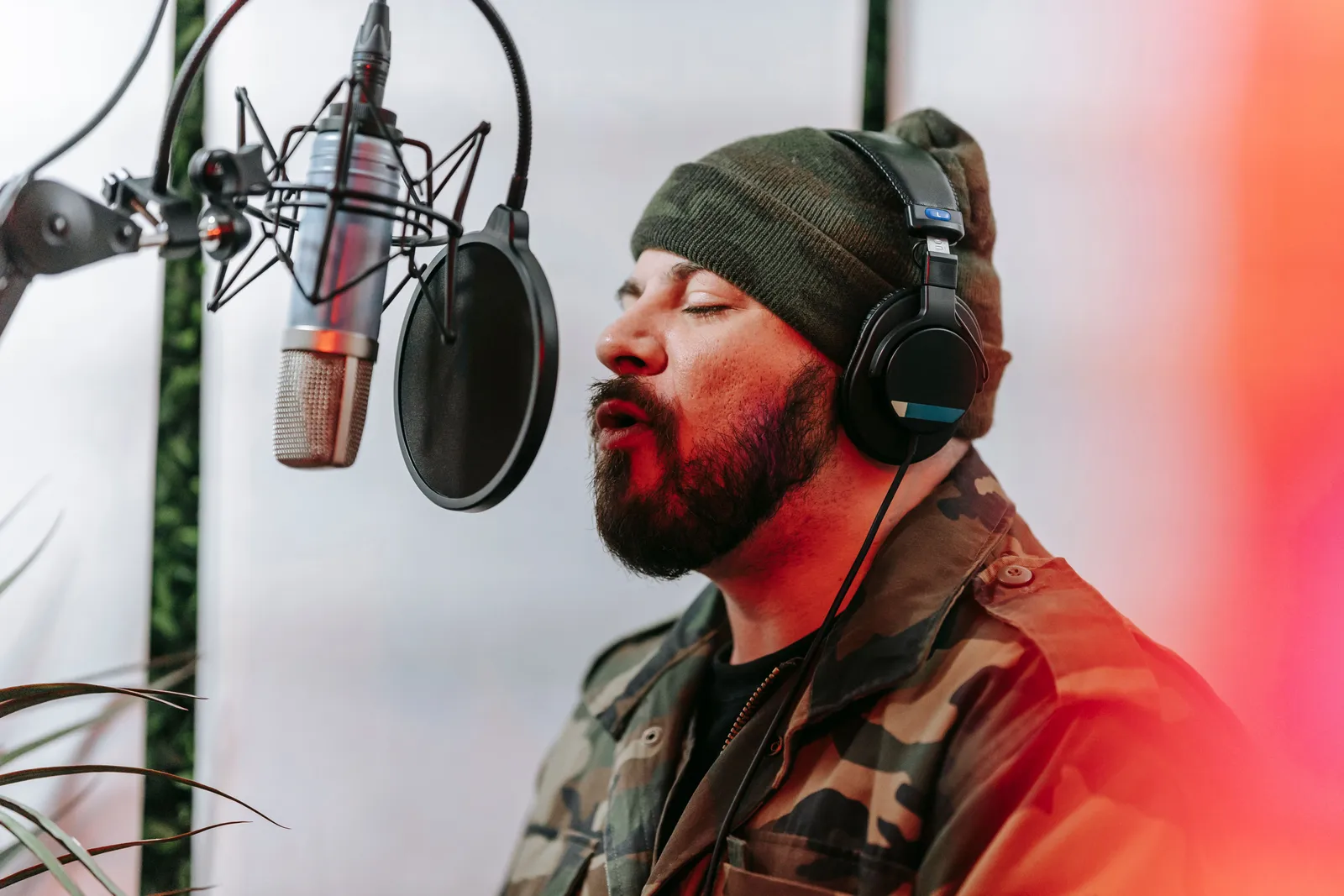 Bearded man in camouflage jacket singing into a microphone in a studio setting