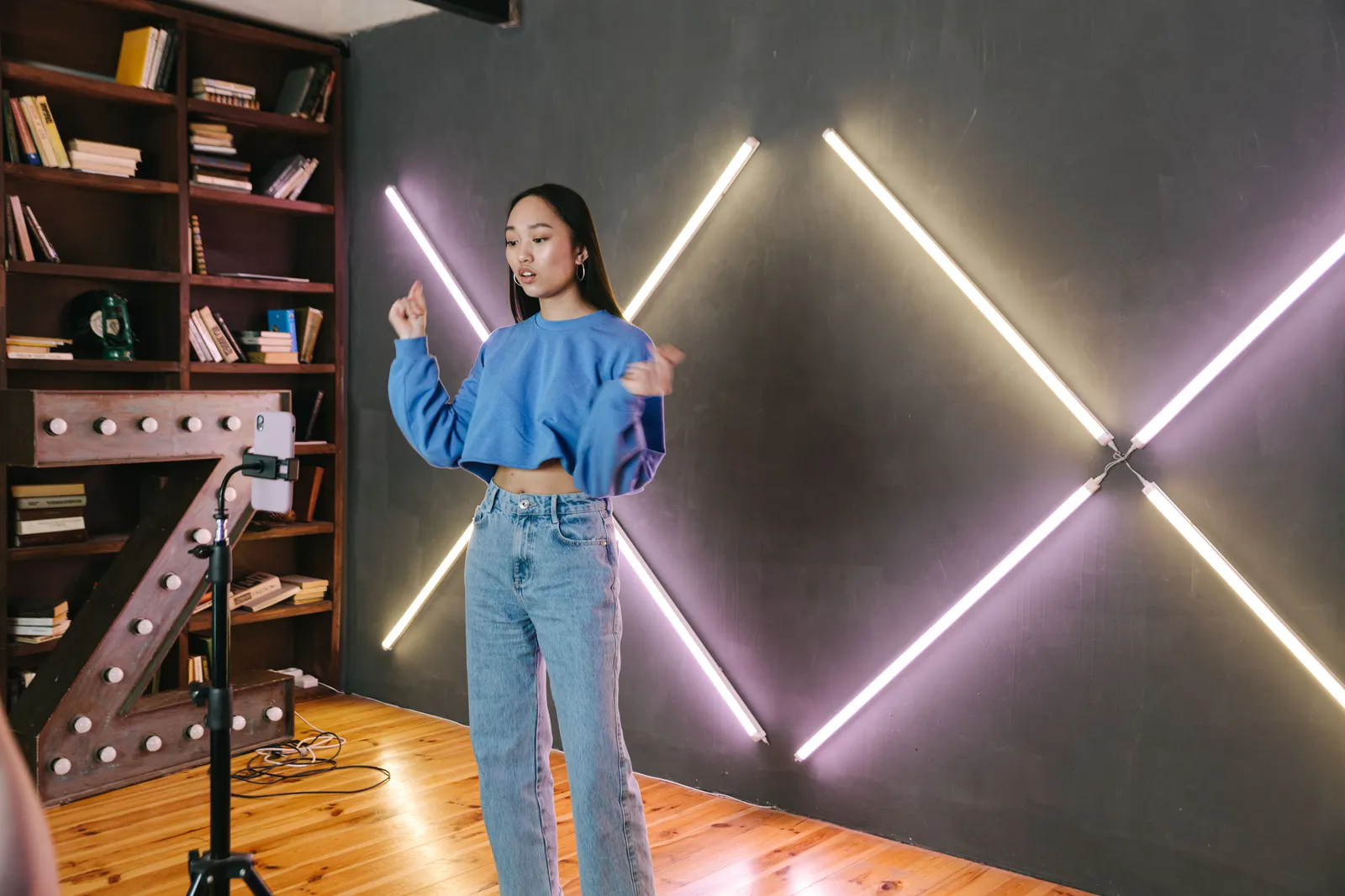Woman filming video content in a trendy room with neon lighting and bookshelves