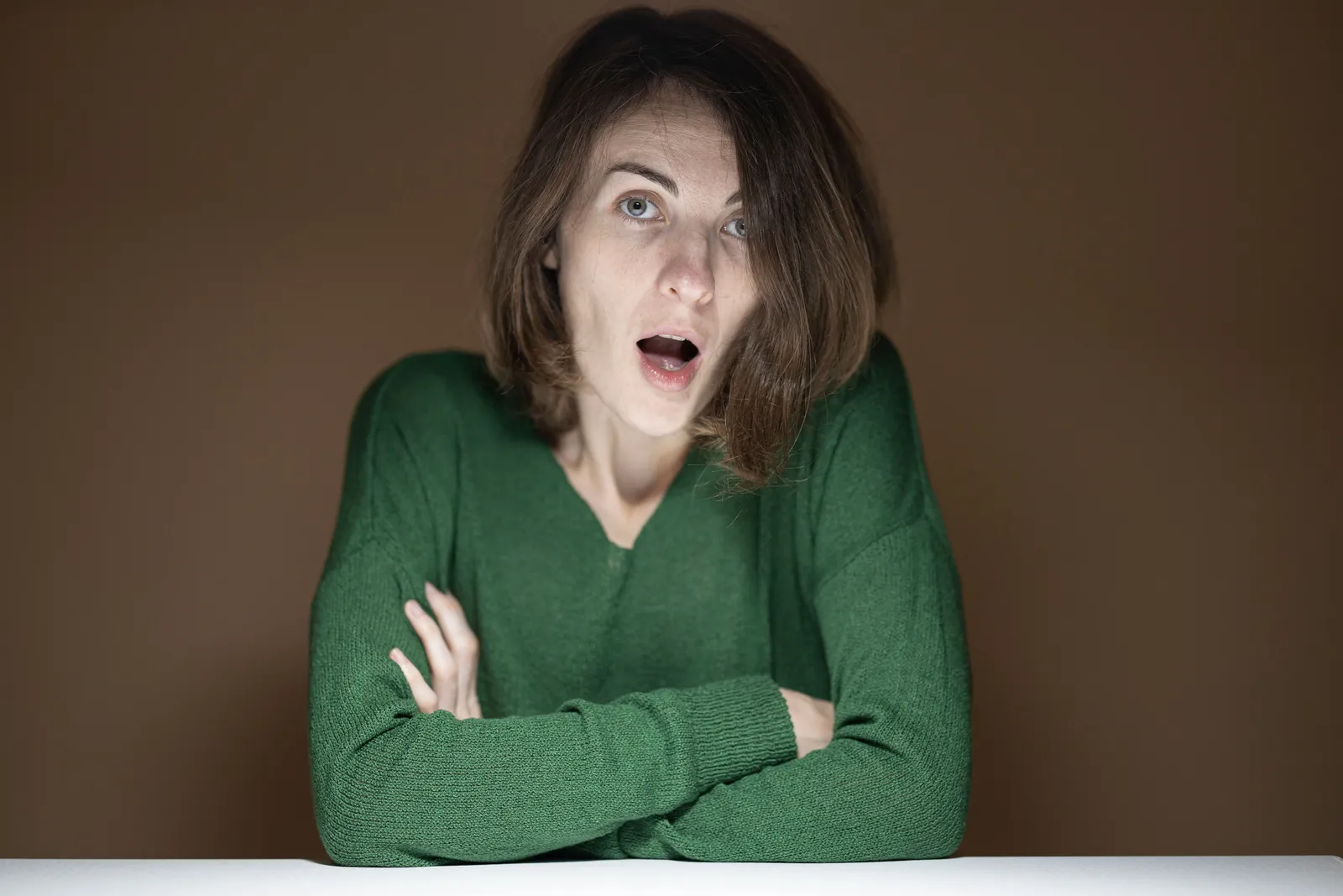 Close-up of a woman with a surprised expression wearing a green sweater indoors