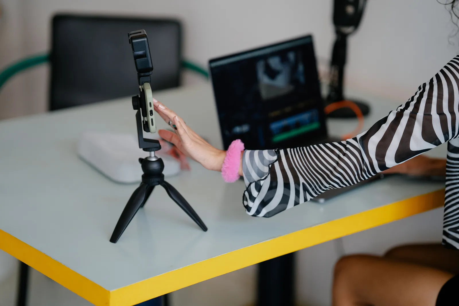 Woman adjusting smartphone on tripod with laptop setup for video editing