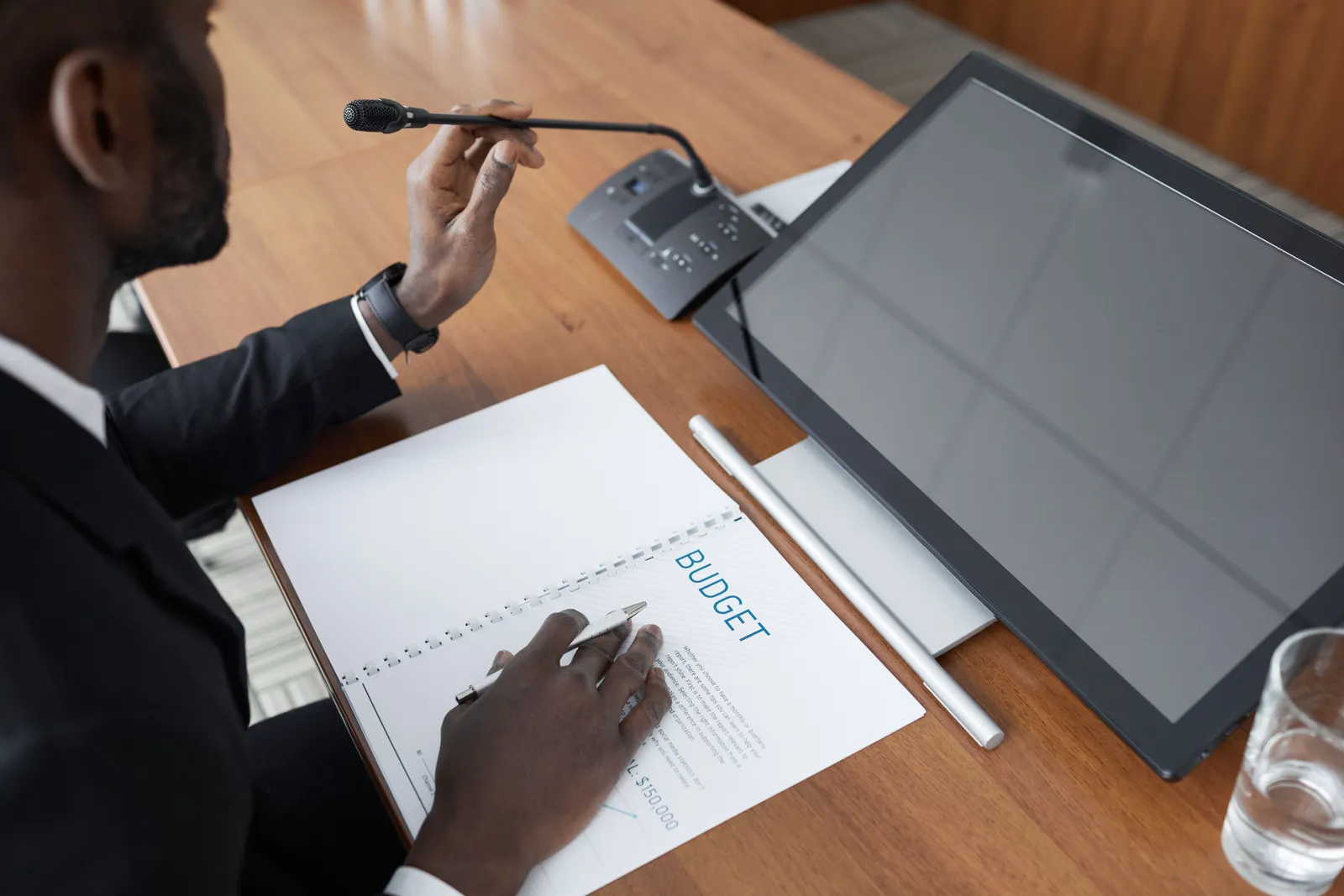 Man in a meeting reviewing a budget document with a microphone