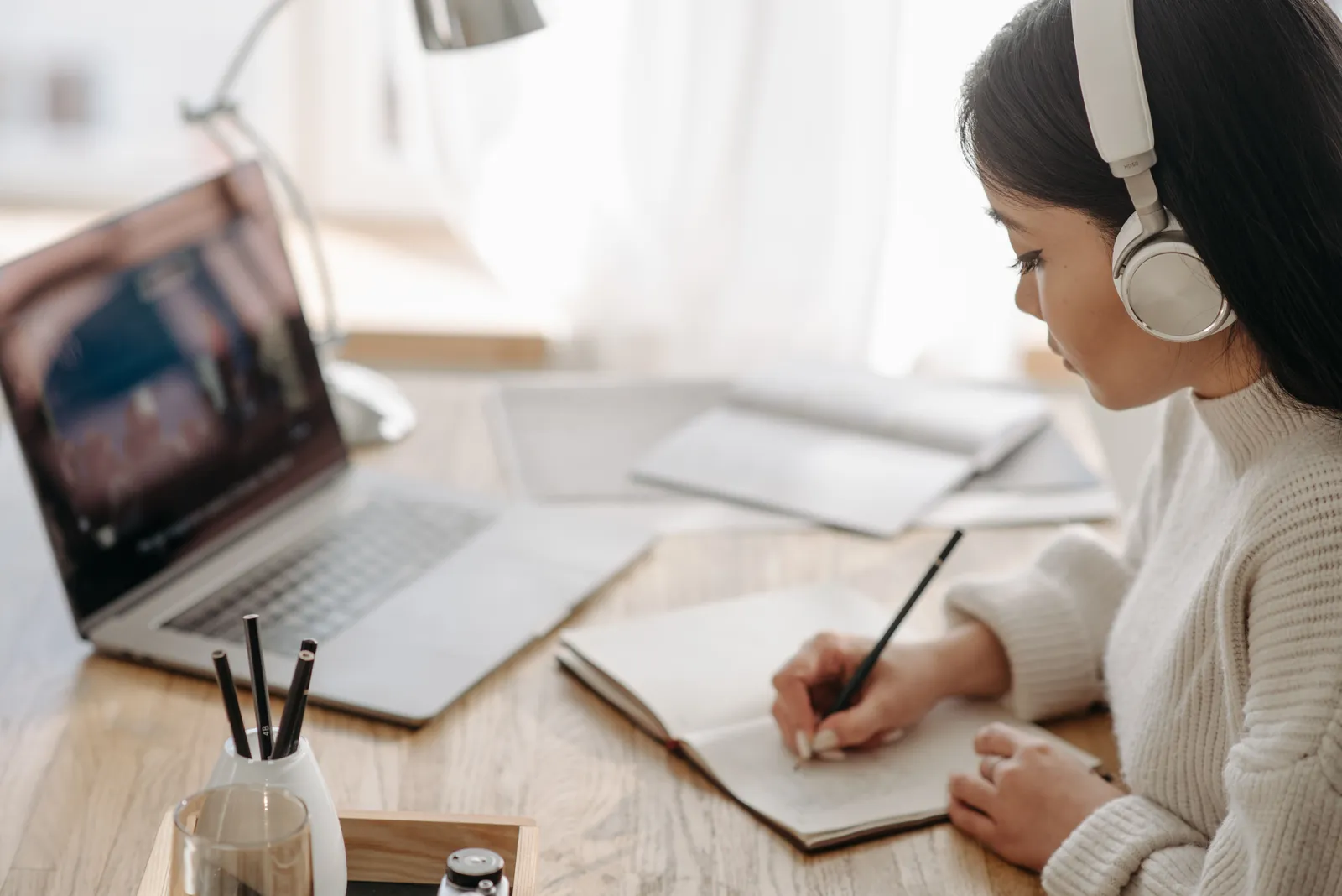 Woman focused on study, writing notes during online session at home with laptop and headphones