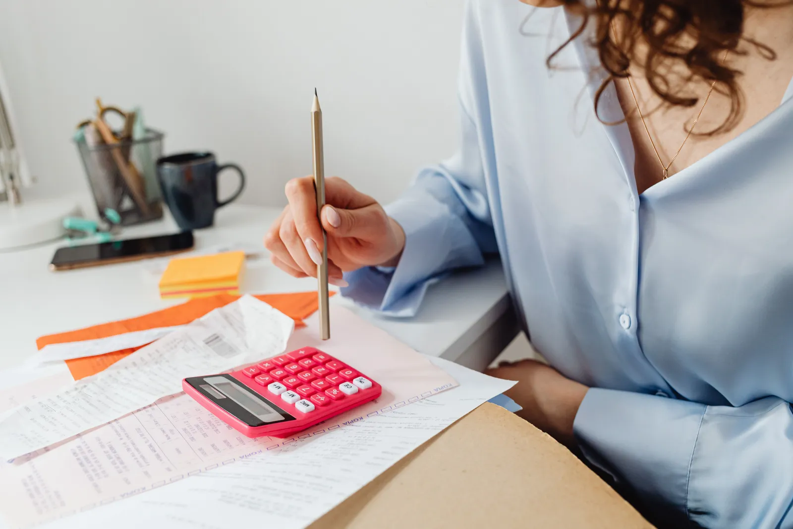 A woman is calculating expenses using a calculator and papers at her desk