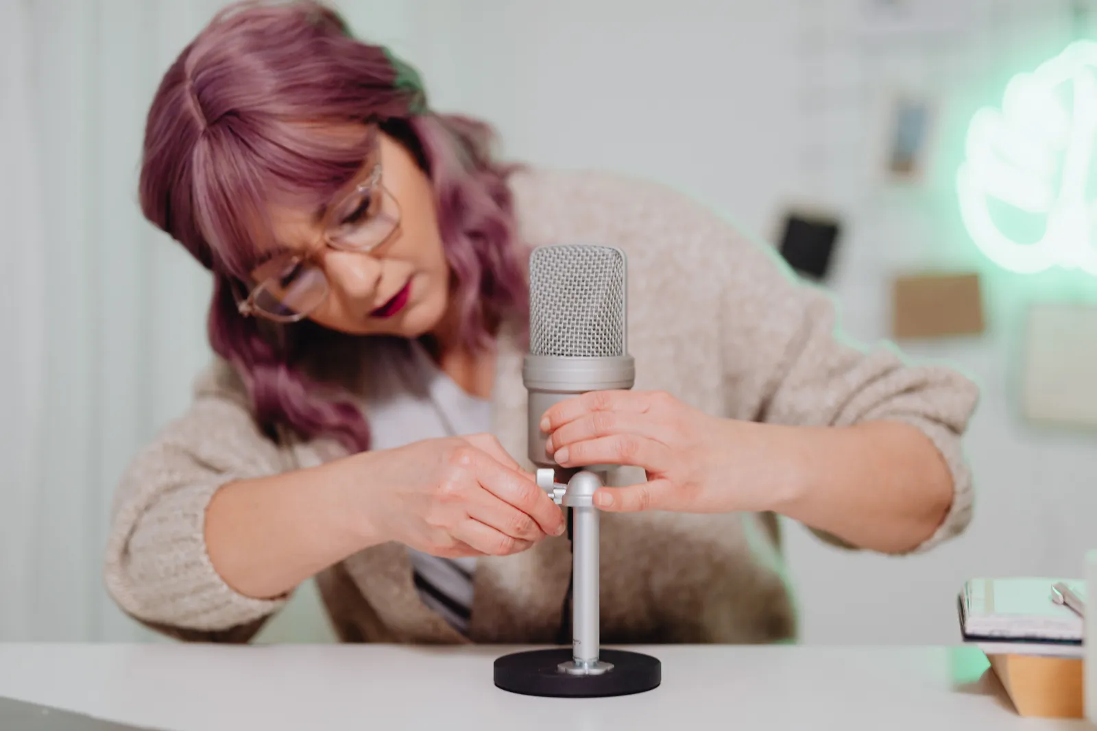 Woman with dyed hair adjusts a microphone in a cozy indoor setting, creating a relaxed atmosphere