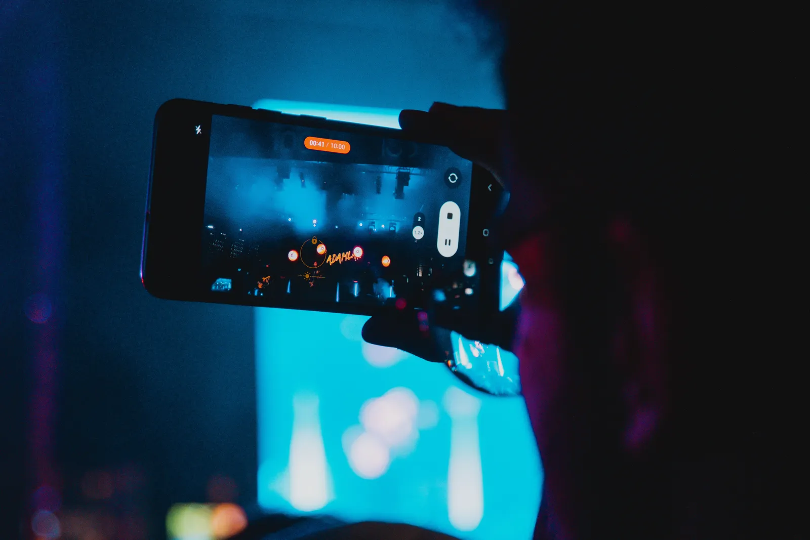 Close-up of a person filming a concert with a smartphone, capturing vibrant stage lights and atmosphere
