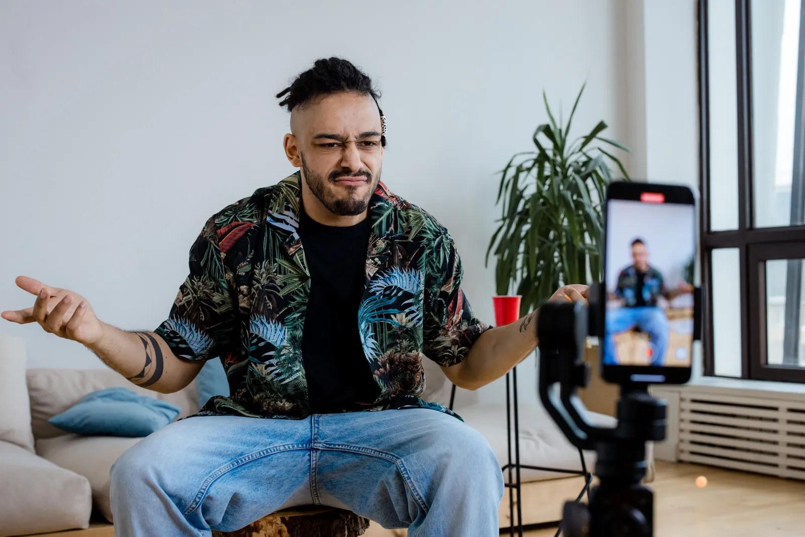 Casual man vlogging in a modern living room using smartphone on tripod, expressing thoughts