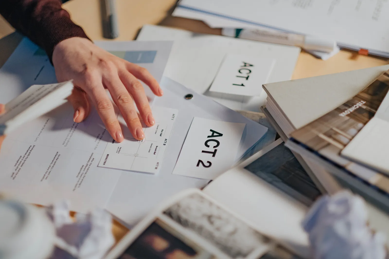 A cluttered desk with scripts, notes, and a person's hand organizing screenplay drafts