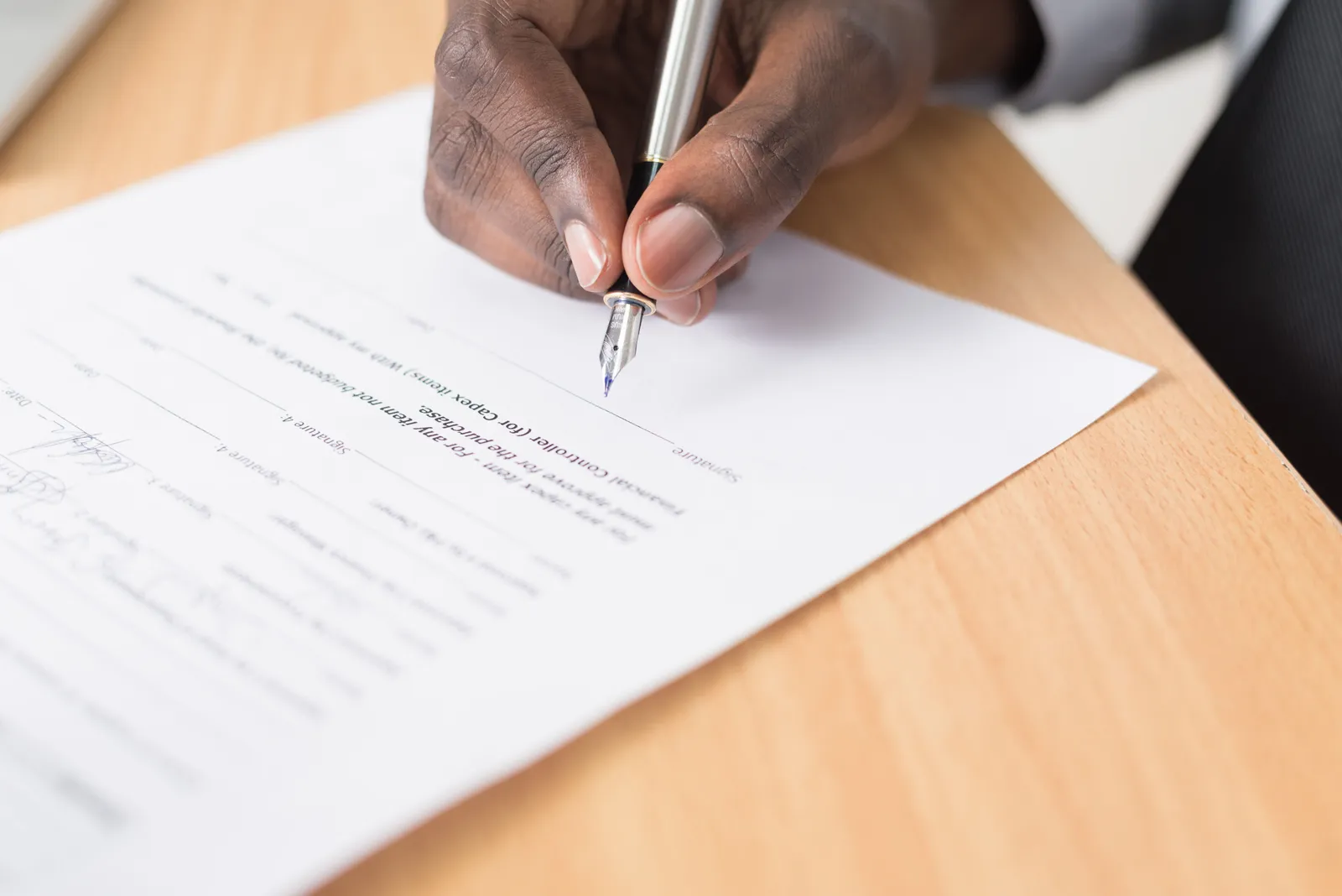 A hand holding a pen signing a document close-up on a desk, symbolizing agreement or contract finalization