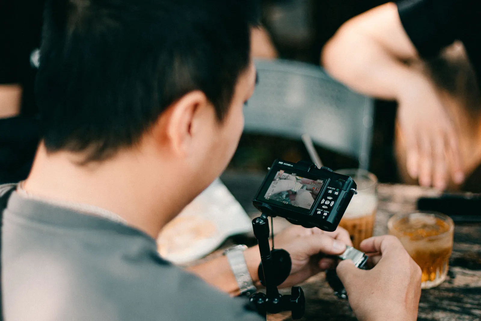 A man adjusting his camera at a caf茅 table, capturing coffee drinks outdoors