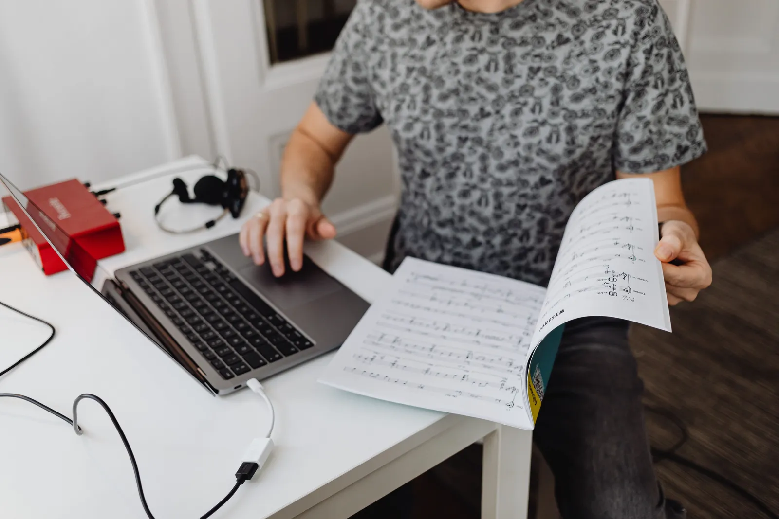 A person typing on a laptop while holding music sheets, focused on work