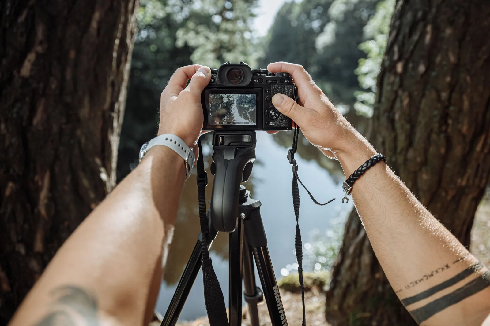 Hands holding a camera on a tripod focusing on a scenic outdoor landscape between two trees