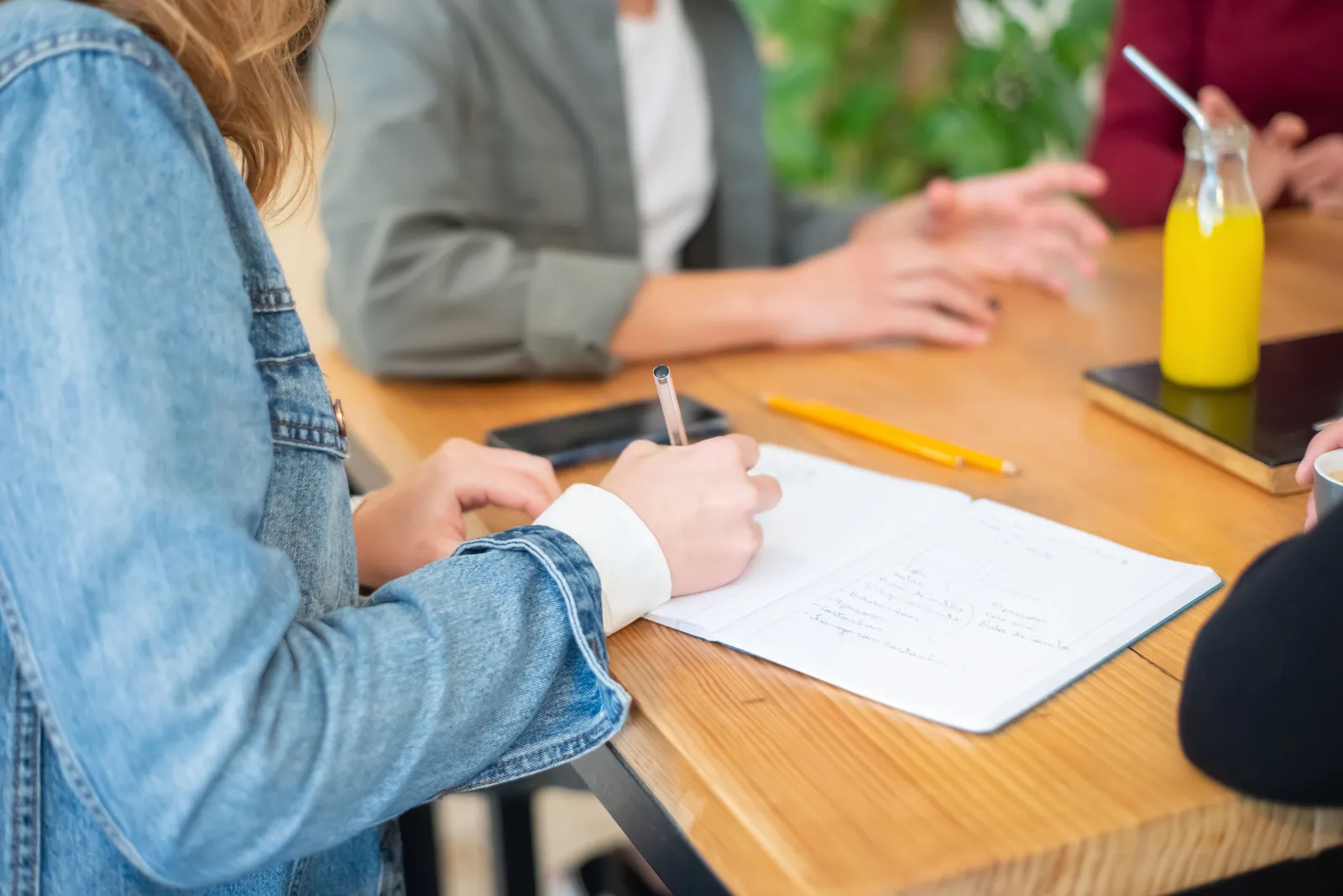 Collaborative meeting with adults writing notes on a wooden table, featuring a casual setting