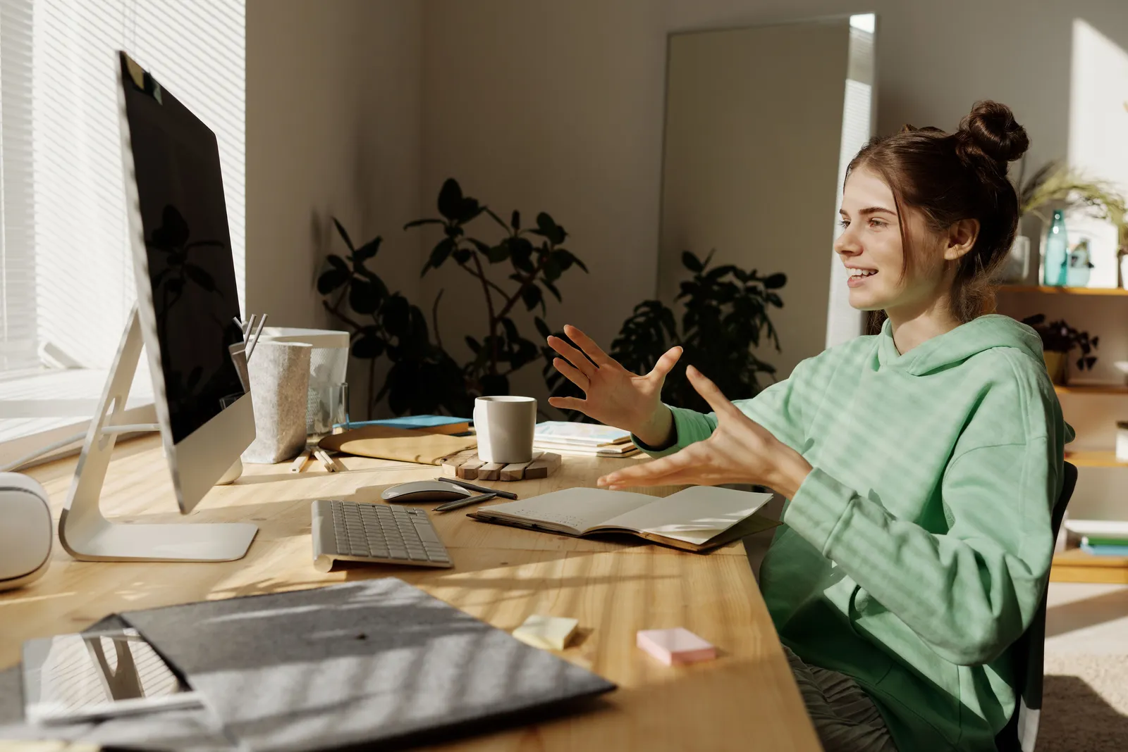 A woman in a green hoodie having a video call at her home office desk