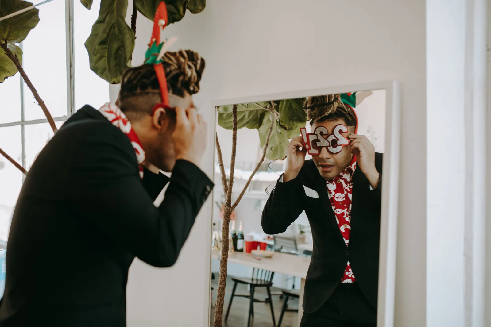 Man in festive costume adjusts party glasses in front of a mirror, embodying New Year celebrations