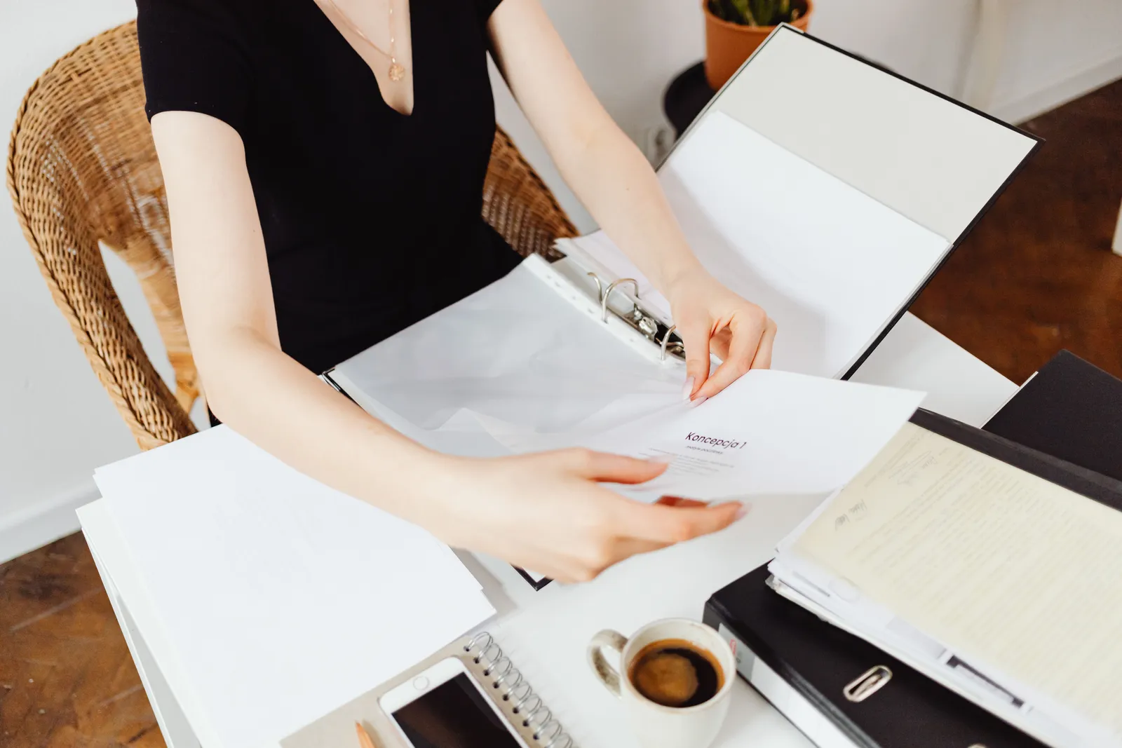 A woman seated at a desk organizing documents in an office setting with coffee and smartphone nearby