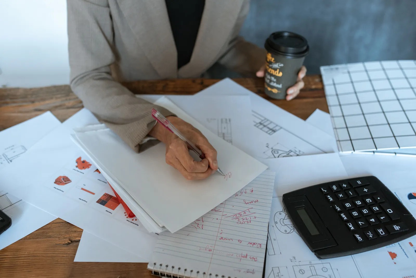 Close-up of a person writing at an office desk with documents and coffee, symbolizing productivity