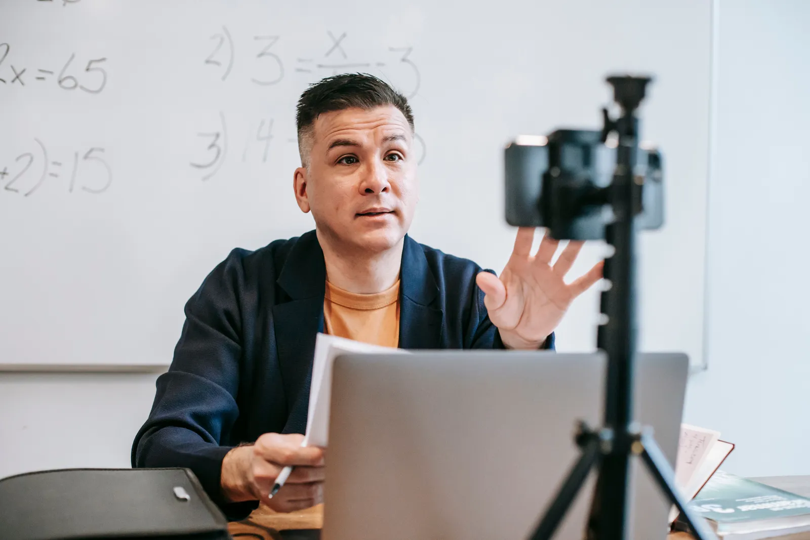A male instructor conducting an online teaching session using a laptop and camera setup