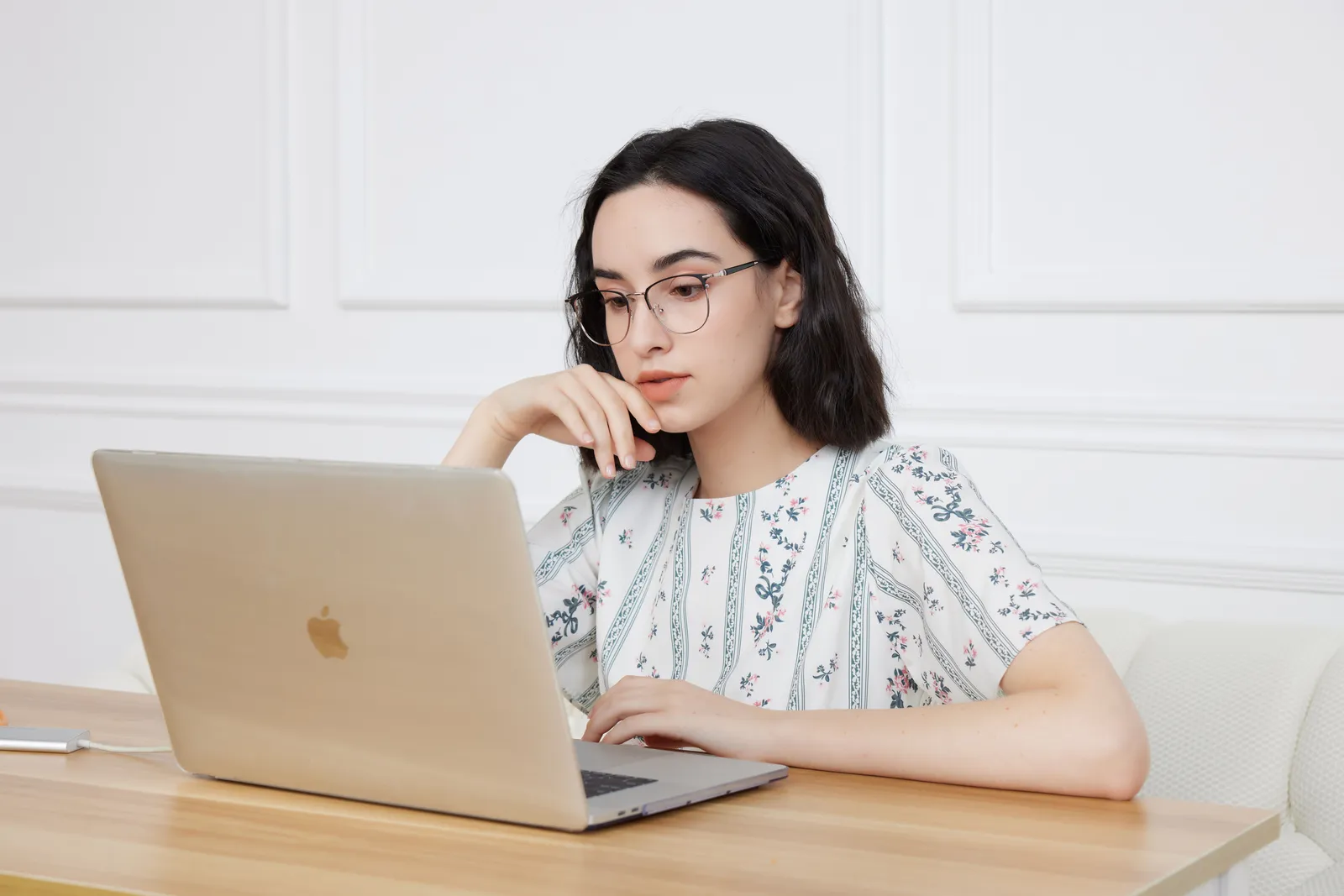 Woman in floral blouse wearing glasses, focused on laptop work at home