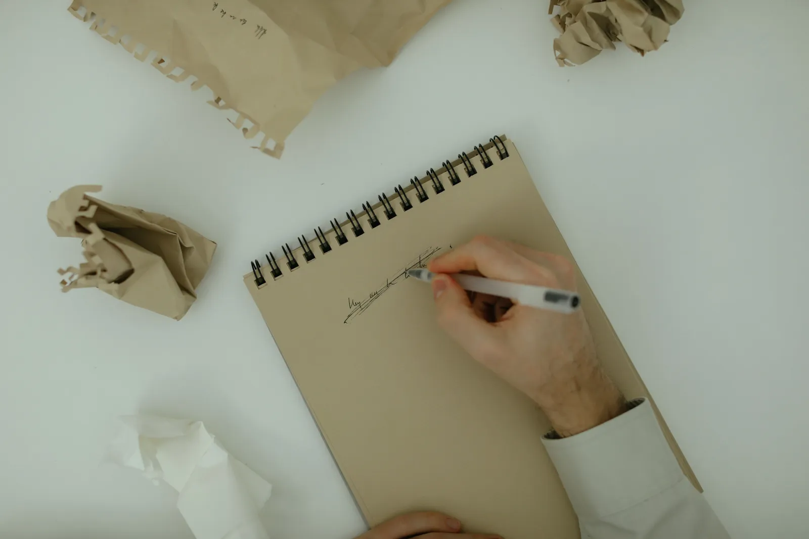 Person writing on a notepad surrounded by crumpled paper, symbolizing brainstorming and creativity