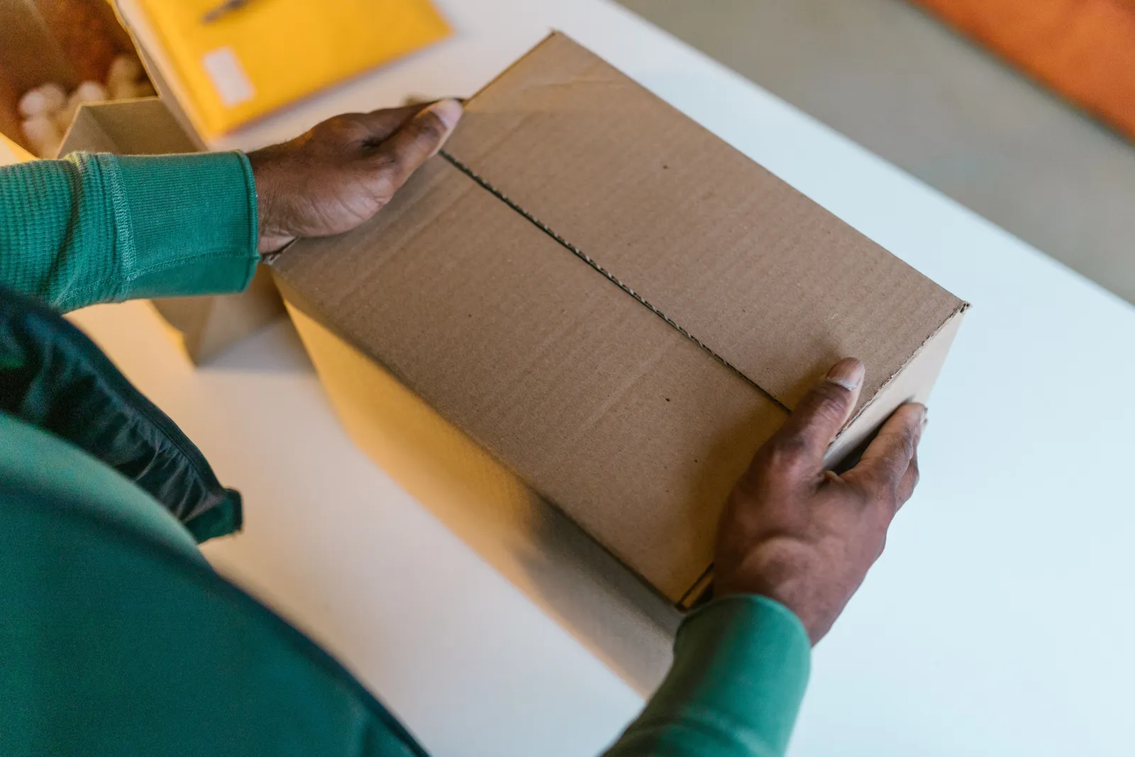 Close-up of hands holding a brown cardboard box on a white table indoors