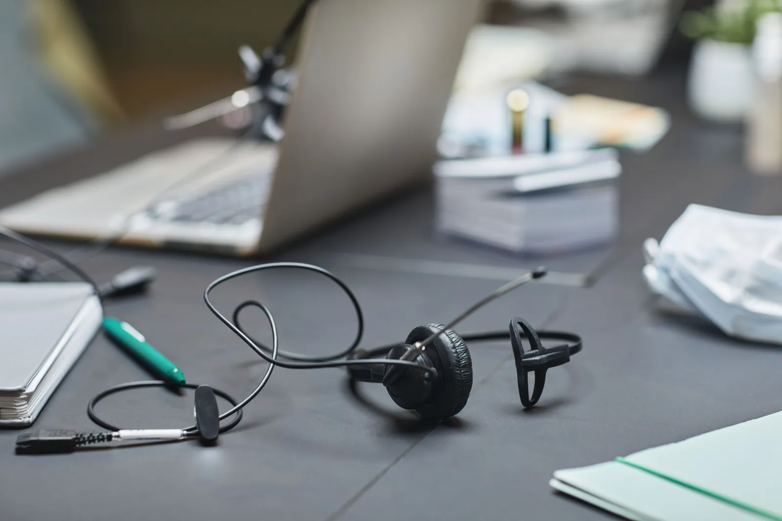 A close-up of office desk featuring a laptop, headset, and stationery, ideal for business settings