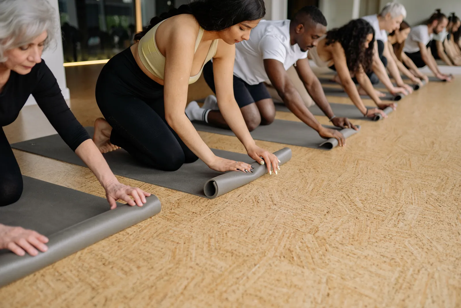 A diverse group of adults rolling yoga mats in a studio before practice, promoting fitness and wellbeing
