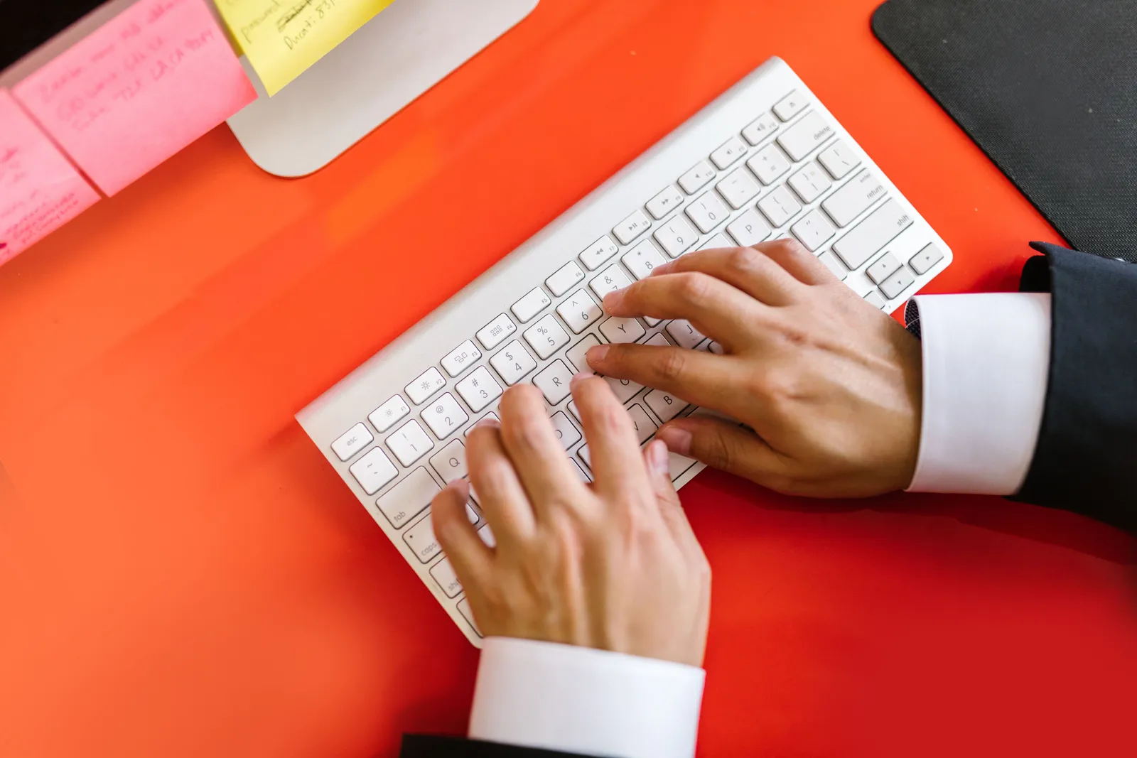 Close-up of hands typing on a wireless keyboard on an orange desk, ideal for tech and business themes