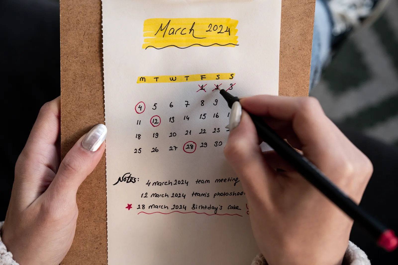 Close-up of a woman's hands organizing a planner for March 2024 with handwritten notes and highlights