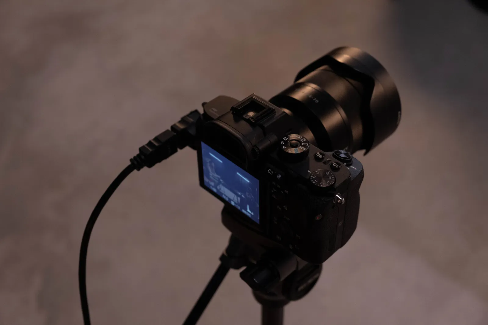 Detailed view of a professional camera setup on a tripod indoors, showcasing its screen and cables
