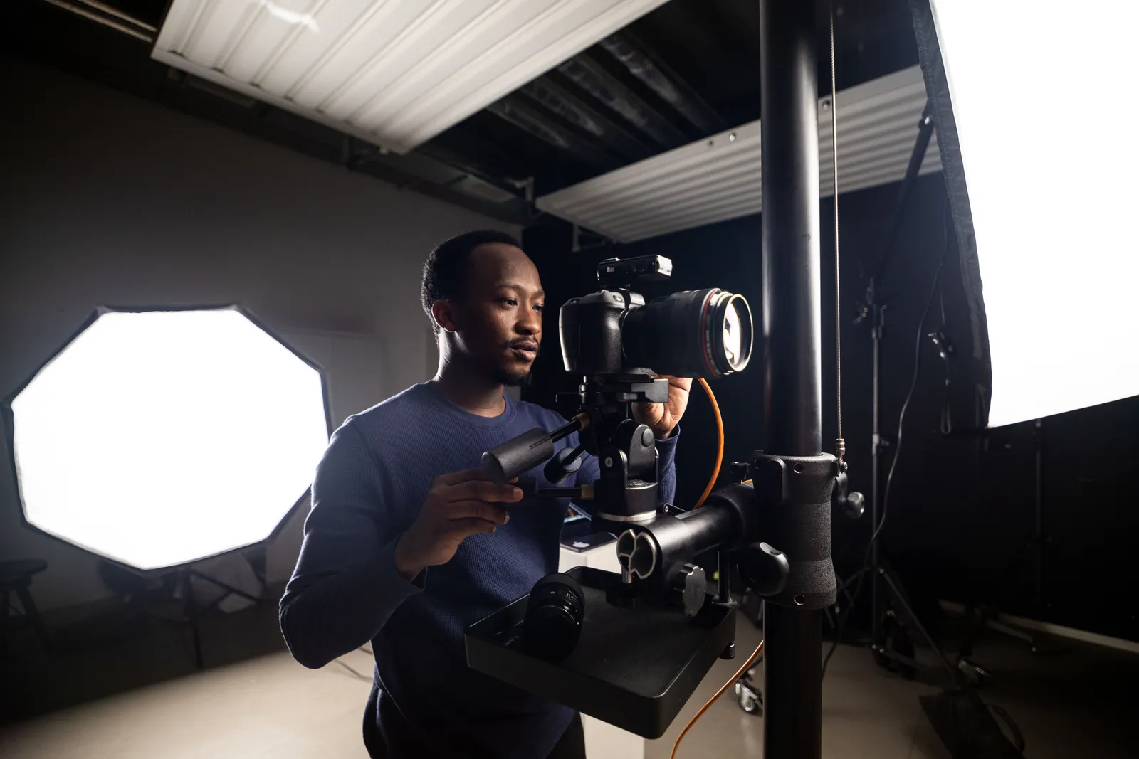 Photographer adjusting camera in studio, surrounded by lighting equipment